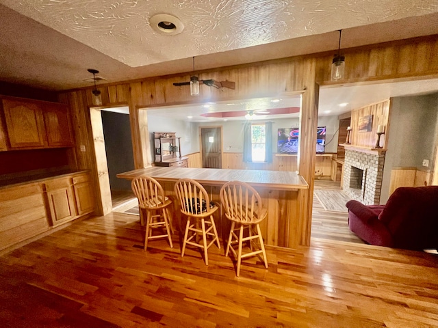 kitchen with light wood-type flooring, a fireplace, hanging light fixtures, a kitchen bar, and a textured ceiling