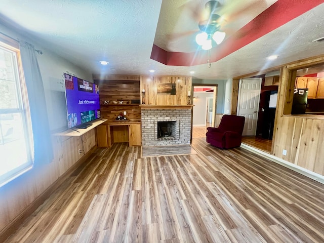 unfurnished living room with wood-type flooring, a textured ceiling, wood walls, and ceiling fan