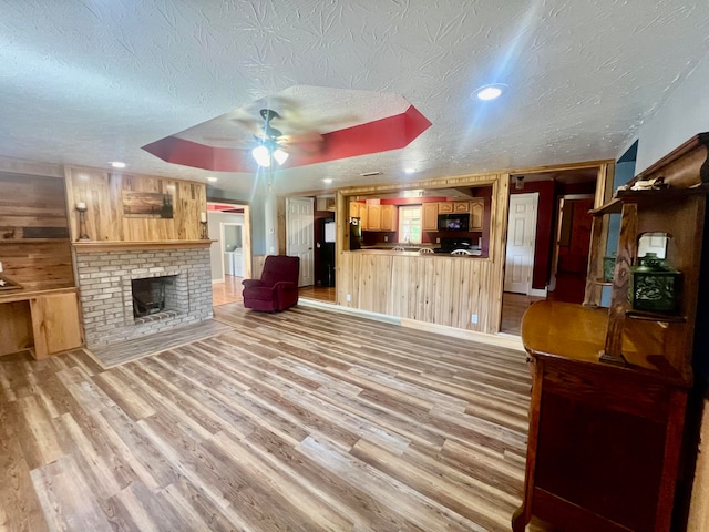 living room featuring hardwood / wood-style flooring, wooden walls, ceiling fan, and a textured ceiling