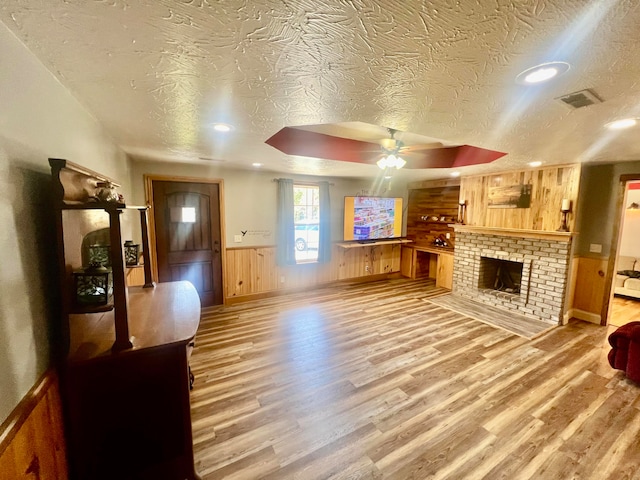 living room featuring wood-type flooring, a textured ceiling, wooden walls, and ceiling fan