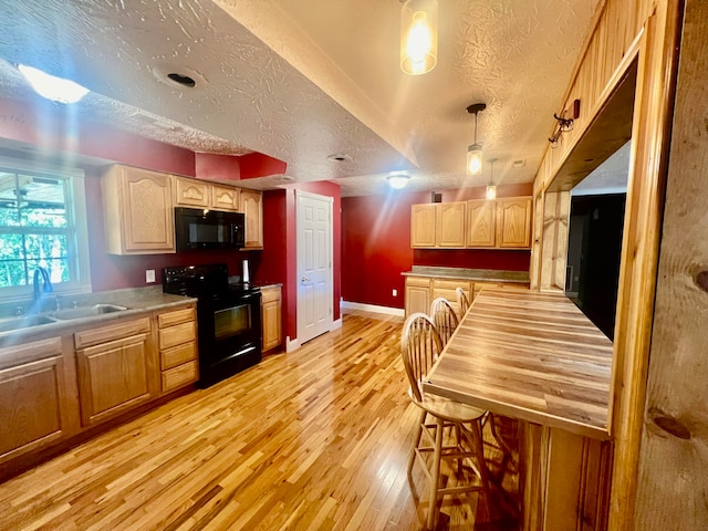 kitchen featuring a textured ceiling, light wood-type flooring, hanging light fixtures, and black appliances