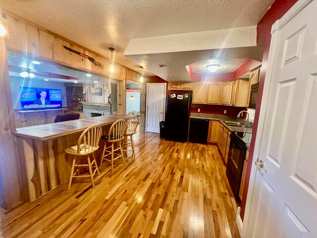 kitchen featuring light wood-type flooring, black appliances, sink, a kitchen breakfast bar, and a textured ceiling