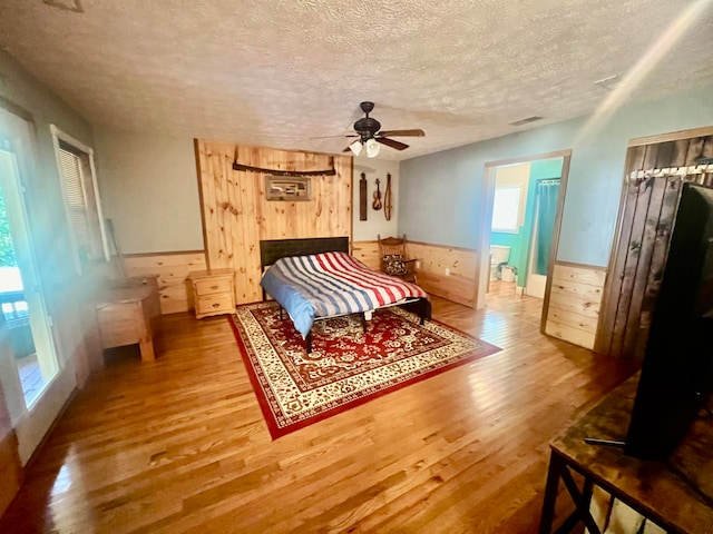 bedroom with wood walls, wood-type flooring, ceiling fan, and a textured ceiling