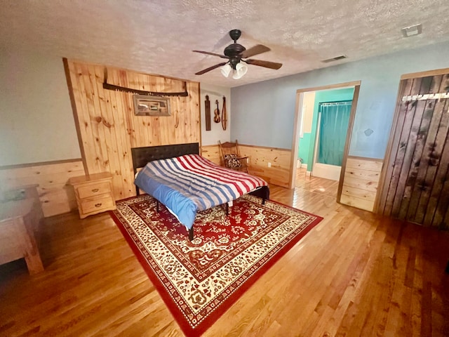 bedroom with wood-type flooring, ceiling fan, wooden walls, and a textured ceiling