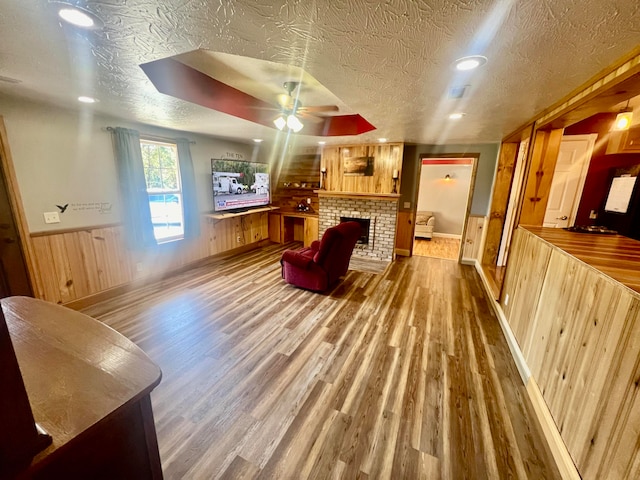 living room with ceiling fan, a textured ceiling, wooden walls, hardwood / wood-style flooring, and a fireplace