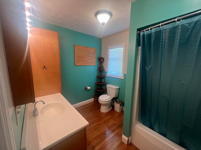 full bathroom featuring vanity, hardwood / wood-style flooring, shower / bath combo with shower curtain, toilet, and a textured ceiling