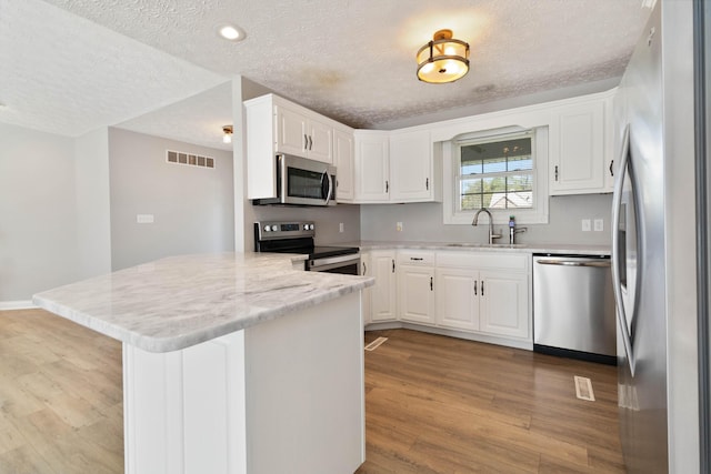 kitchen with visible vents, a sink, light wood-style floors, a textured ceiling, and stainless steel appliances