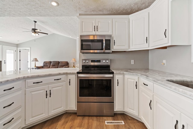 kitchen with a textured ceiling, a ceiling fan, light wood-style floors, lofted ceiling, and stainless steel appliances
