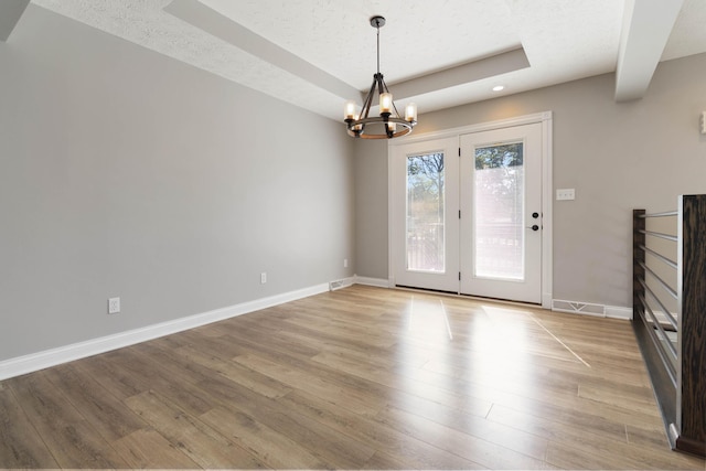 unfurnished dining area featuring baseboards, an inviting chandelier, a textured ceiling, light wood-style floors, and a tray ceiling