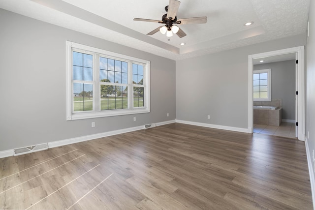 empty room with baseboards, visible vents, a tray ceiling, ceiling fan, and wood finished floors