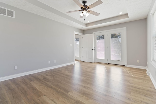 spare room featuring a tray ceiling, light wood finished floors, baseboards, and a ceiling fan