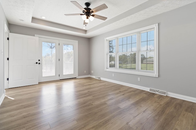 empty room featuring a tray ceiling, wood finished floors, plenty of natural light, and visible vents