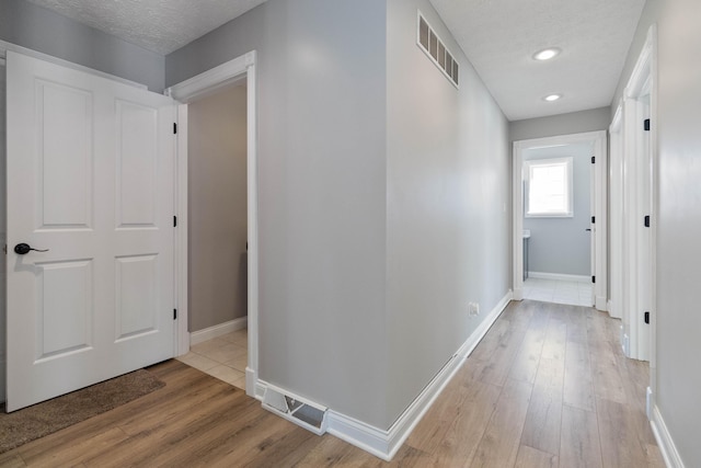 corridor featuring light wood-style floors, baseboards, and visible vents