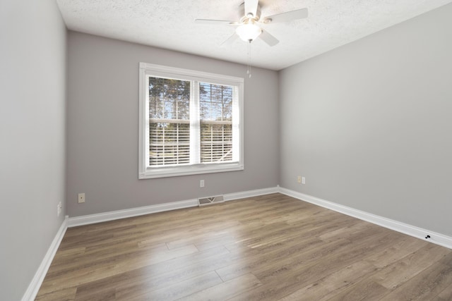 spare room with a textured ceiling, wood finished floors, ceiling fan, and visible vents