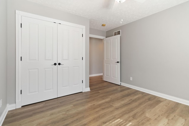 unfurnished bedroom featuring visible vents, baseboards, a closet, and wood finished floors