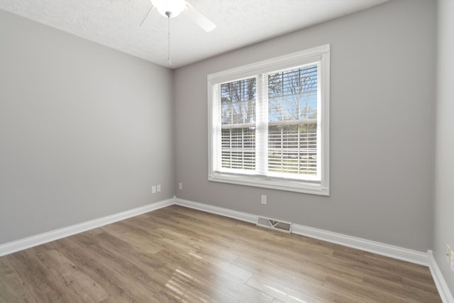 unfurnished room featuring visible vents, baseboards, a ceiling fan, a textured ceiling, and wood finished floors