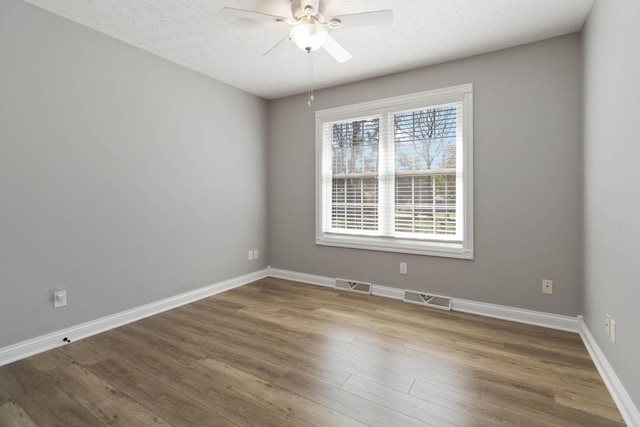 spare room featuring wood finished floors, baseboards, a ceiling fan, and visible vents