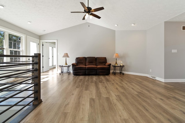 living room with baseboards, a ceiling fan, light wood-style floors, visible vents, and lofted ceiling