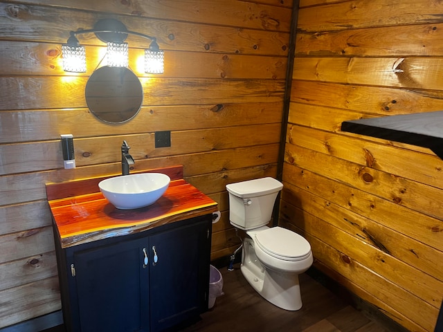 bathroom with hardwood / wood-style floors, toilet, wood walls, and vanity