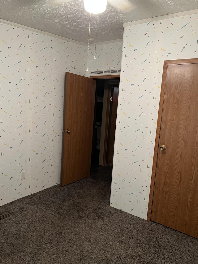 spare room with dark colored carpet, visible vents, and a textured ceiling