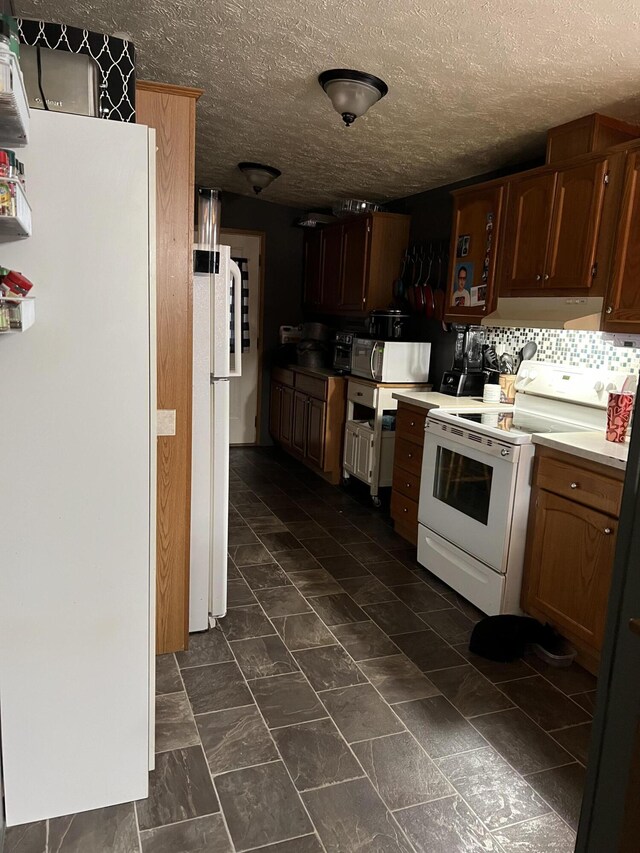 kitchen featuring under cabinet range hood, white appliances, light countertops, backsplash, and brown cabinets