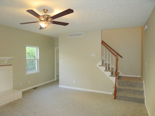 unfurnished living room featuring ceiling fan, a tile fireplace, and light colored carpet