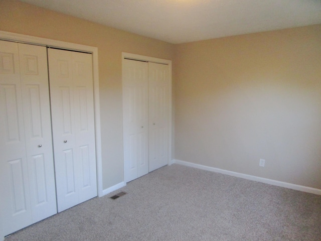 unfurnished bedroom with carpet floors and two closets