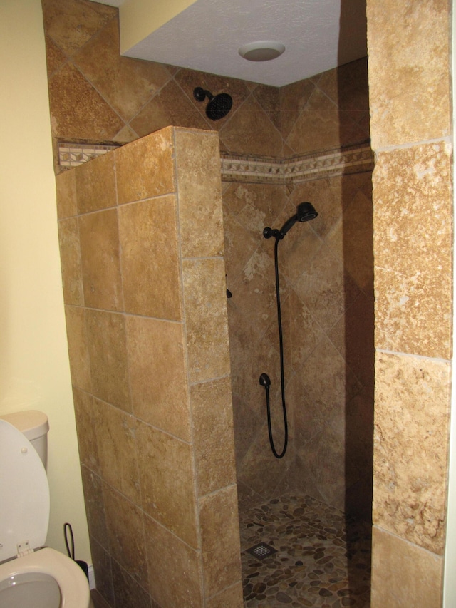 bathroom with a textured ceiling, tiled shower, and toilet