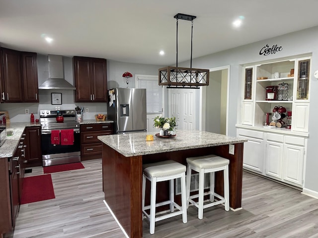 kitchen featuring light wood-type flooring, wall chimney range hood, appliances with stainless steel finishes, hanging light fixtures, and a center island