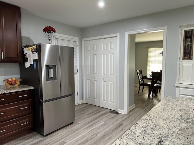 kitchen with light wood-type flooring, stainless steel refrigerator with ice dispenser, dark brown cabinetry, and light stone countertops