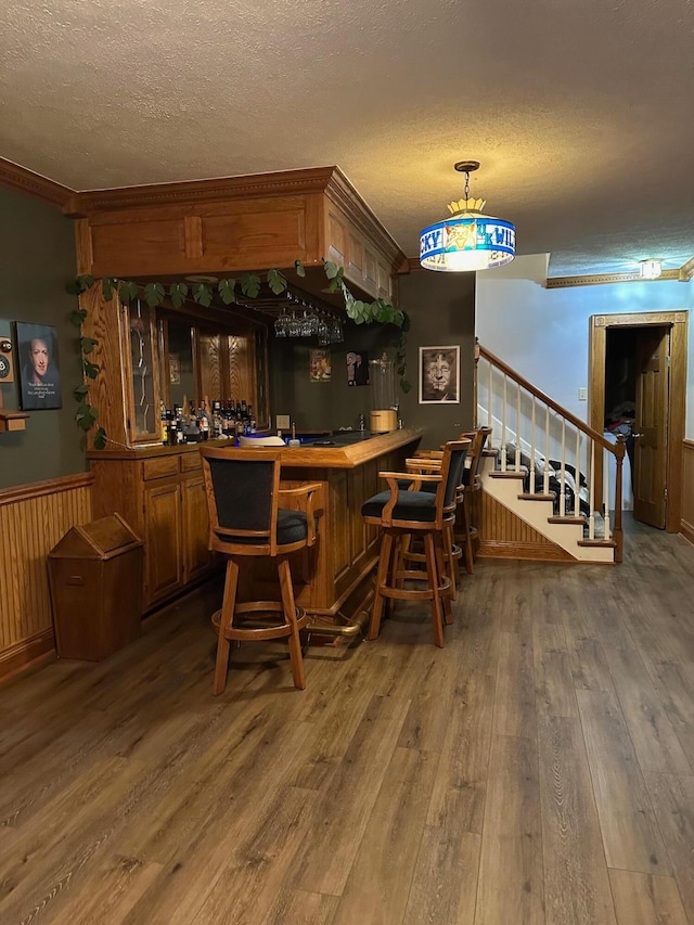 bar with dark wood-type flooring, wood walls, a textured ceiling, and decorative light fixtures