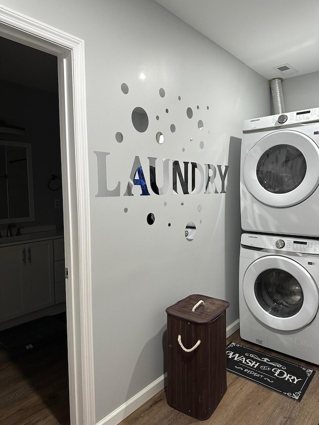 clothes washing area featuring hardwood / wood-style floors and stacked washer / drying machine