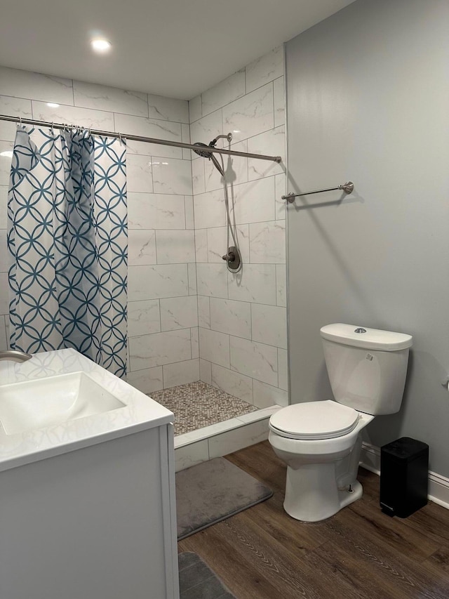 bathroom with tiled shower, hardwood / wood-style flooring, toilet, and vanity