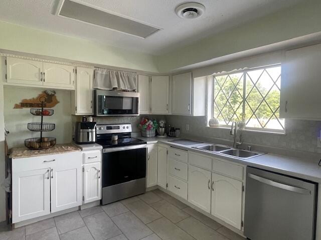 kitchen with sink, decorative backsplash, appliances with stainless steel finishes, light tile patterned floors, and white cabinetry