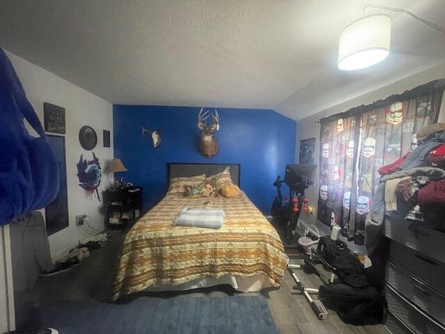 bedroom with vaulted ceiling, hardwood / wood-style floors, and a textured ceiling