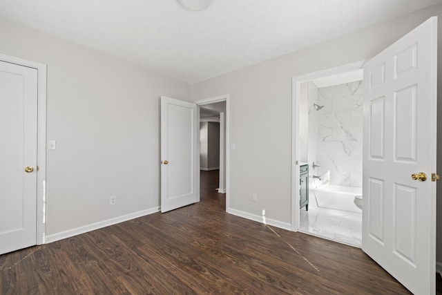 unfurnished bedroom with ensuite bathroom and dark wood-type flooring