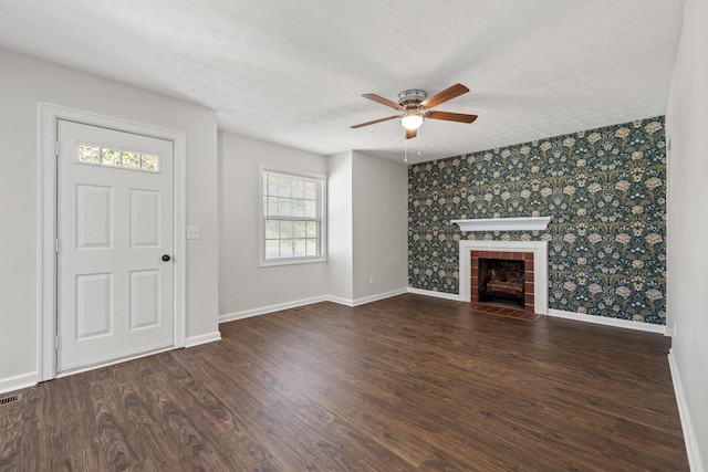 unfurnished living room with ceiling fan, a tiled fireplace, dark hardwood / wood-style floors, and a textured ceiling