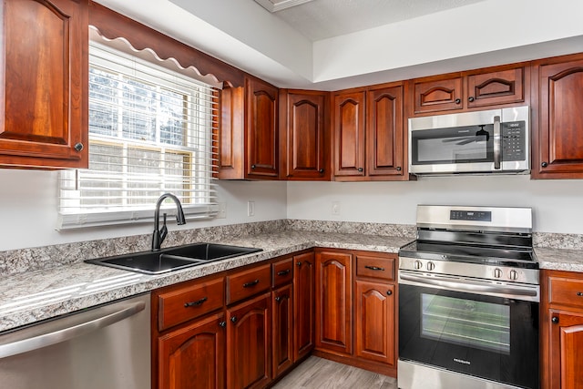 kitchen with a textured ceiling, stainless steel appliances, sink, and light hardwood / wood-style flooring