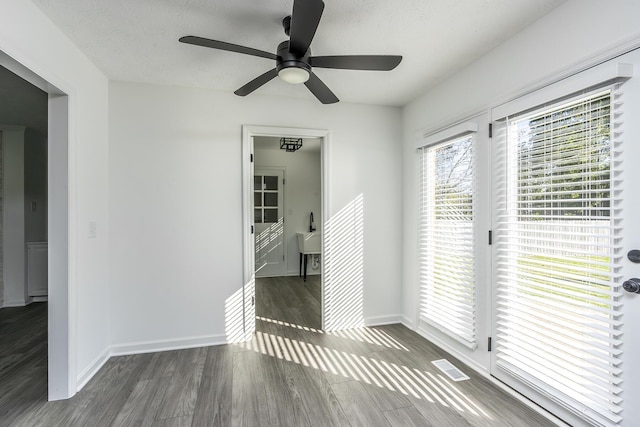 empty room with a ceiling fan, baseboards, visible vents, and wood finished floors
