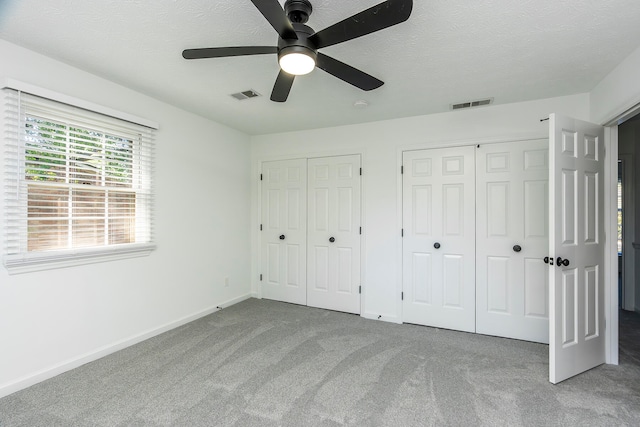 unfurnished bedroom featuring two closets, carpet flooring, a textured ceiling, and ceiling fan