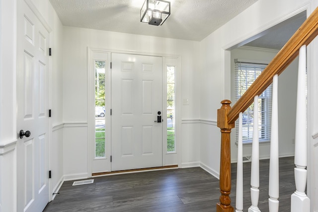 foyer entrance with visible vents, a textured ceiling, dark wood-style floors, and a healthy amount of sunlight