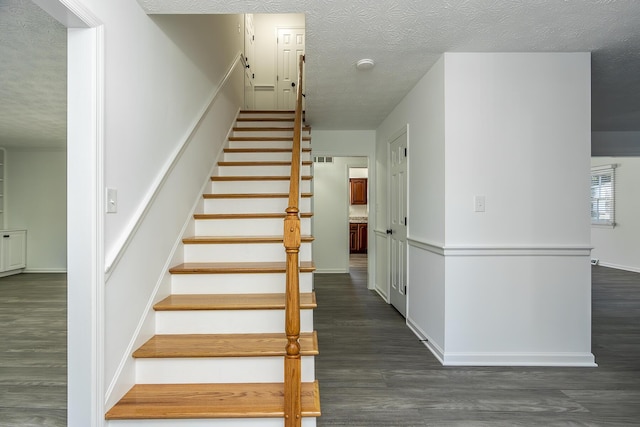 staircase with visible vents, baseboards, a textured ceiling, and wood finished floors
