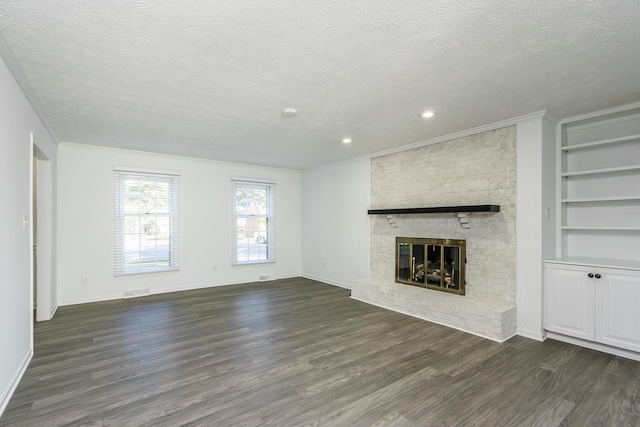 unfurnished living room with dark wood-type flooring, a brick fireplace, ornamental molding, and a textured ceiling