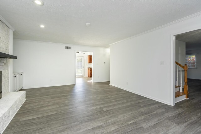 unfurnished living room featuring dark wood-style flooring, visible vents, a fireplace, ornamental molding, and stairs