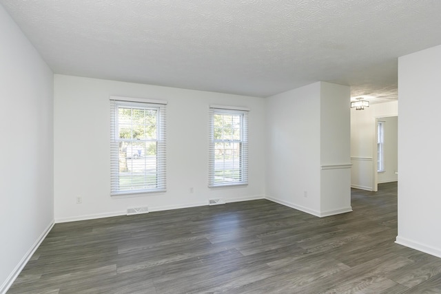 spare room featuring baseboards, dark wood-style floors, a textured ceiling, and visible vents