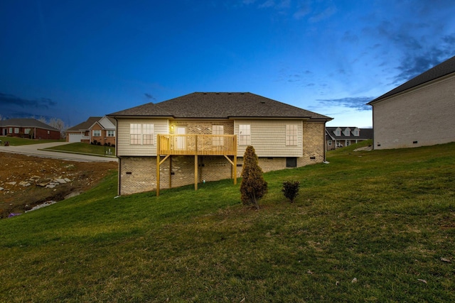 back house at dusk featuring a wooden deck and a lawn