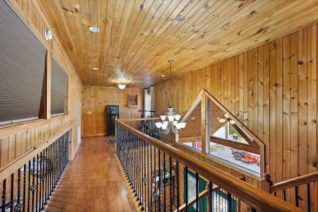 hall with wood-type flooring, a notable chandelier, wood ceiling, and wood walls