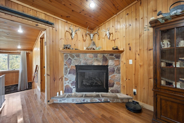 living room with wood walls, wood-type flooring, wooden ceiling, and a stone fireplace