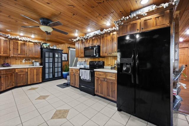 kitchen featuring light tile patterned flooring, black appliances, and wooden walls