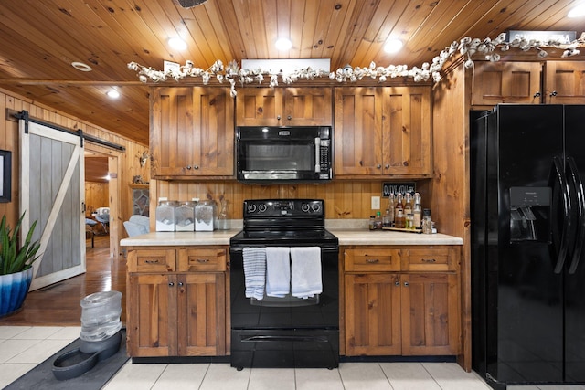 kitchen featuring a barn door, wood ceiling, wooden walls, black appliances, and light tile patterned floors